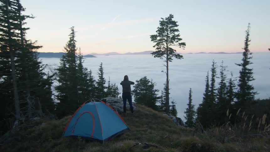 A woman getting out of a tent overlooking a lake