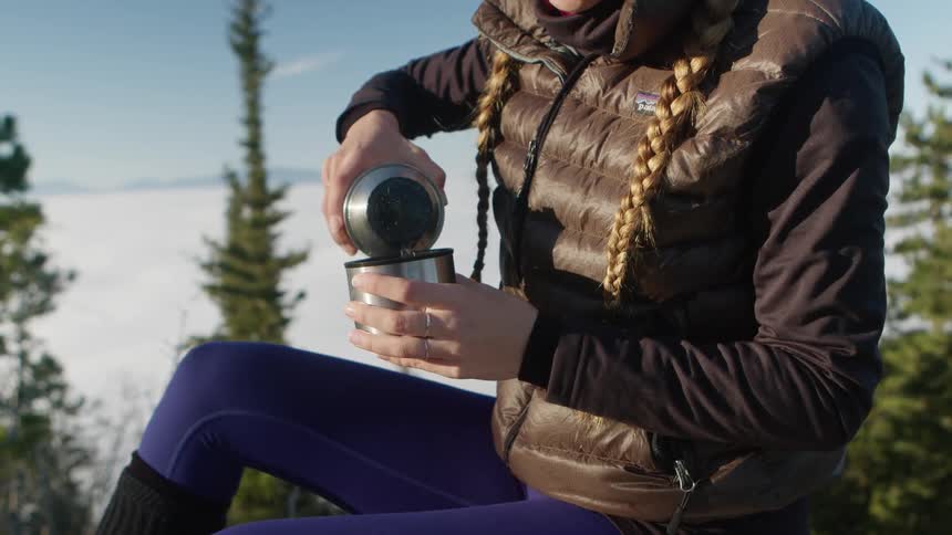 A woman in a forest pours a glass of water from her canister