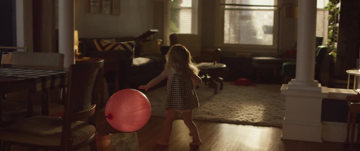 A little girl chases a balloon at home