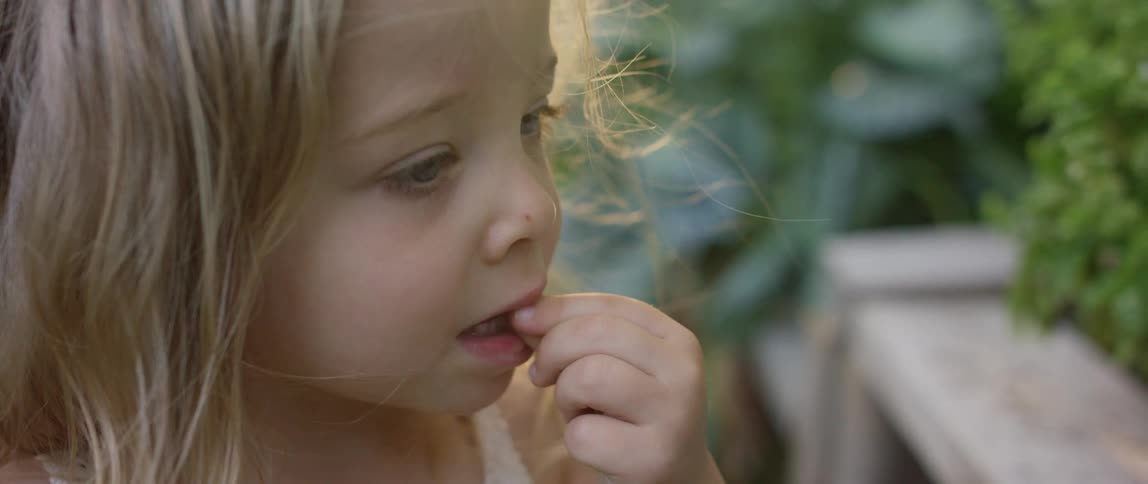 Young blonde girl tasting herbs on a garden at sunset