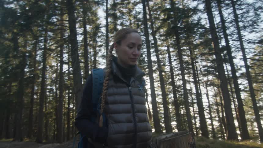 A woman wearing a backpack hikes along in a forest full of tall pine trees