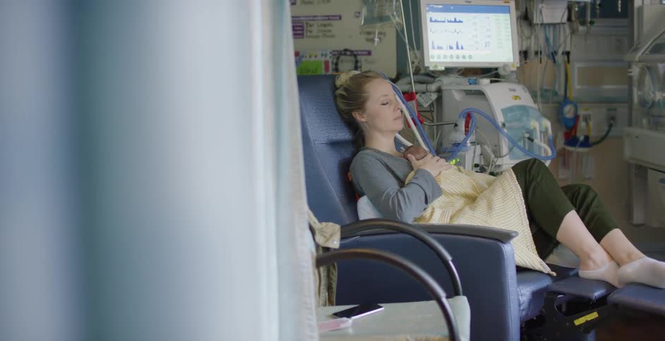 A mother sleeps in a chair while holding her newborn baby in the hospital