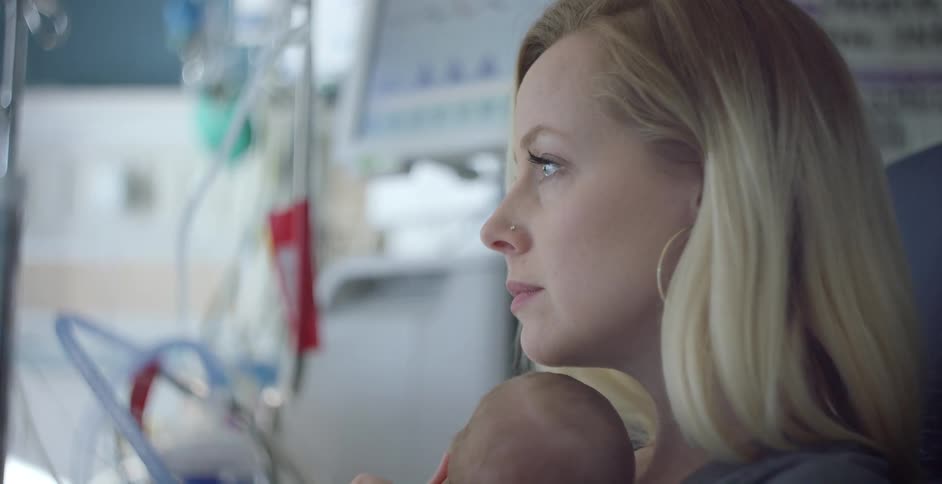 A woman holds her newborn while sitting in a chair in a hospital room
