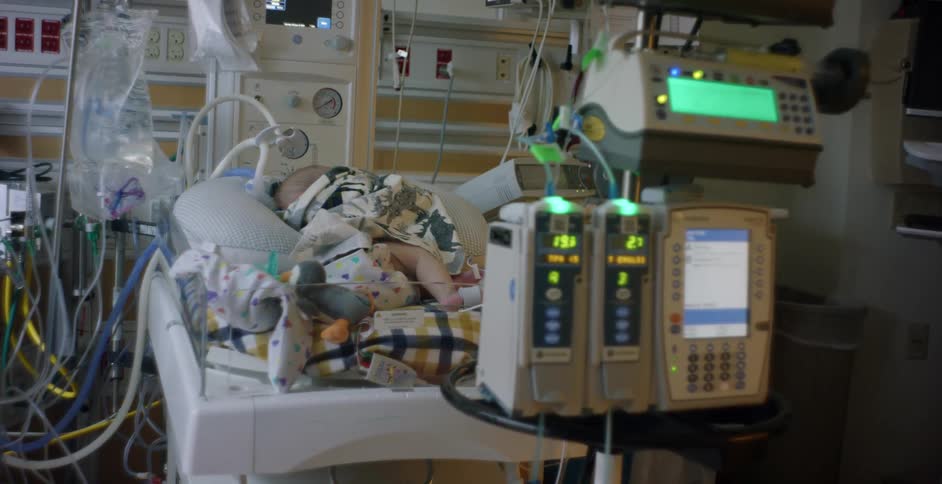 Child lies in hospital bed attached to several machines