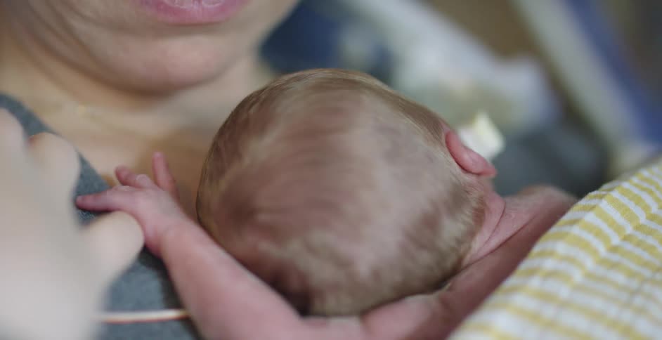 A woman holds a sleeping baby against her chest while resting in a hospital bed