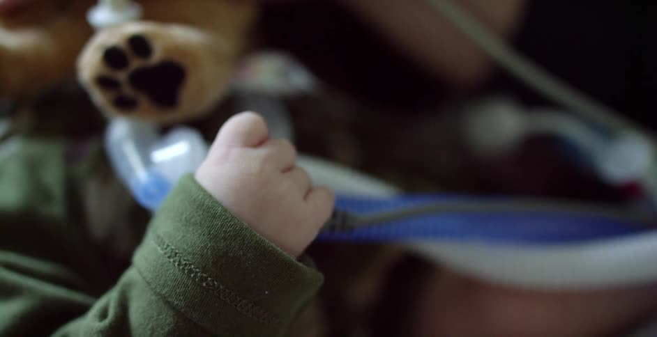 A child hooked up to medical devices while someone is comforting the child with a toy dog
