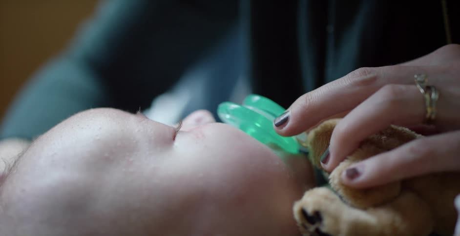 A woman holds a pacifier in a babys mouth while stroking their head gently