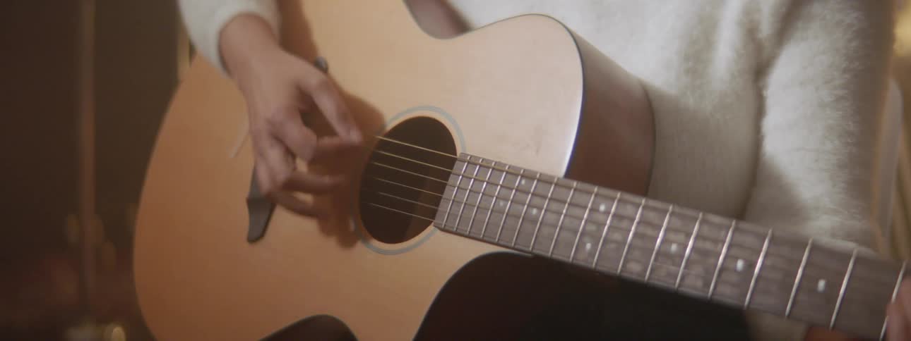 A woman with a sweater playing an acoustic guitar