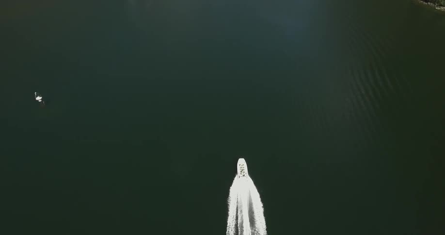 A speedboat seen from overhead, travels down a river in a mountain valley