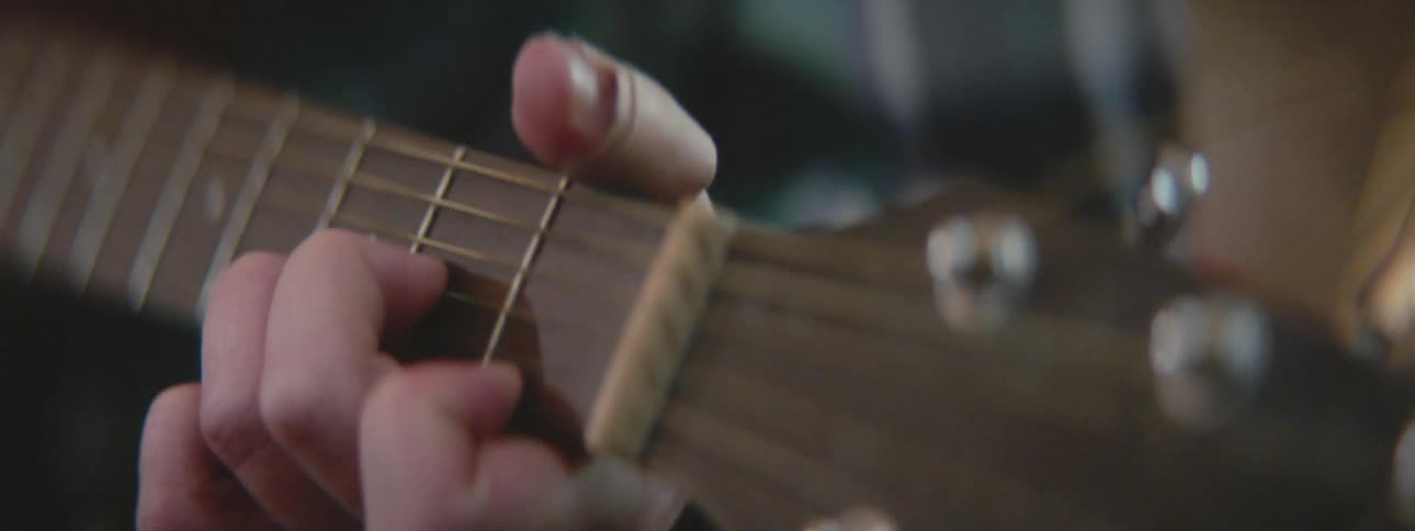 A person plays chords on a guitar with fingers