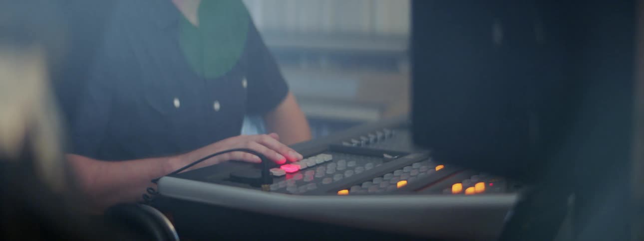 A man sits in front of a control board pressing buttons that illuminate in yellow and red lights