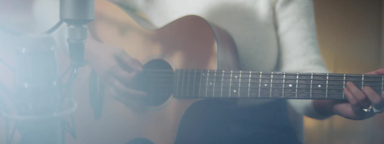A female musician is playing a breedlove guitar in front of a microphone