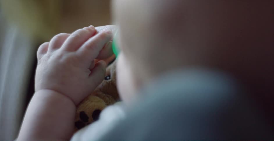 A baby with a toy holding someones finger