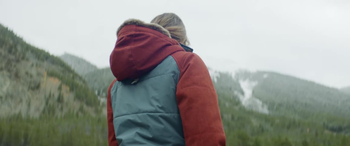 Woman walks in coat outside in front of mountains