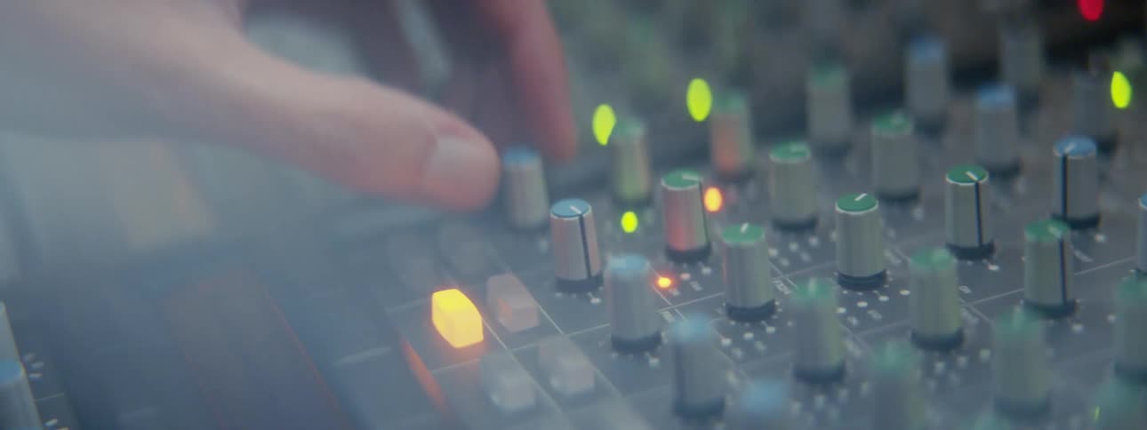 A person adjusts small knobs on a console covered in controls