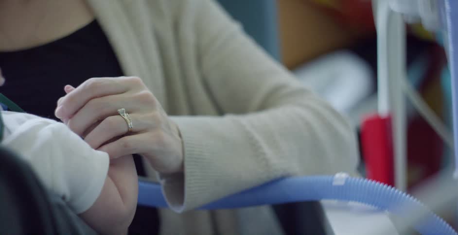 Mother comforts her baby in the hospital by rubbing the arm and holding hands