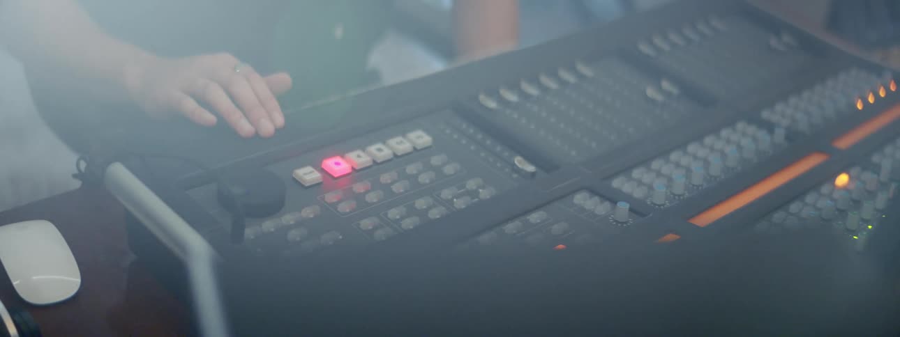 A man sits at a table with an audio board pushing lighted buttons