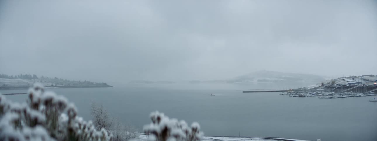 Trees covered in snow next to a lake with the sky and clouds in the background