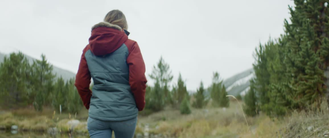 A woman walks alongside a pond in a forest at the base of a mountain on a cold morning