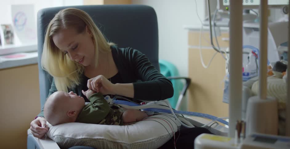 A woman cries and smiles while holding her baby in the hospital as the boy is attached to tubes