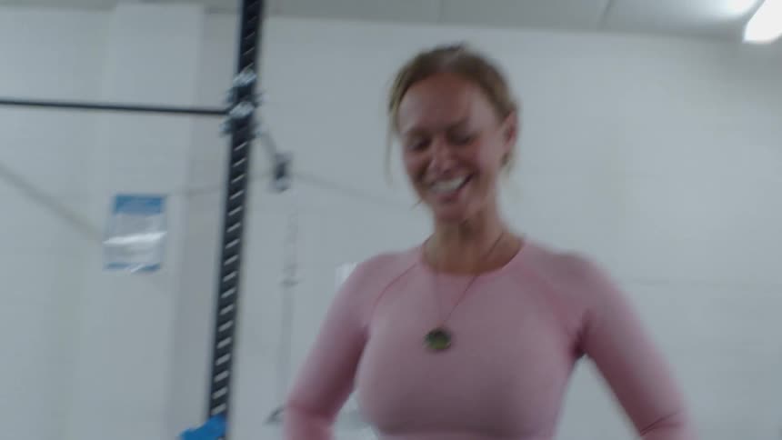 Young fit blonde woman laughs while standing surrounded by equpment inside a gym