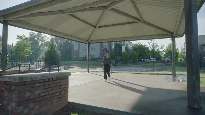 Young woman walking into a gazebo outdoors puts the backpack on the floor