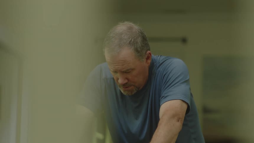 A man in a room exercising on an exercise bike with a wall and doorway in the background