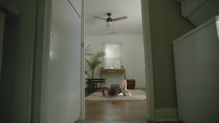 Sports player in exercise clothes doing pushups in a living room while alternating hands resting on a soccer ball