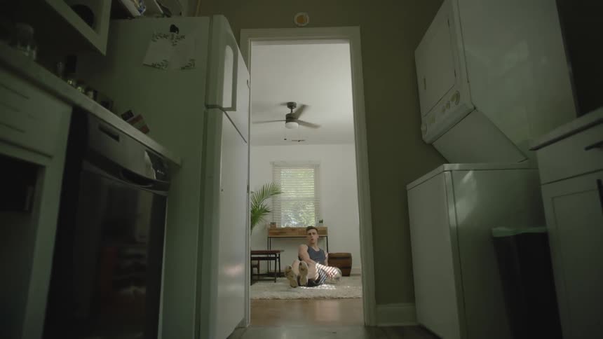 A man sitting on the floor of his home is performing core exercises