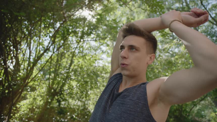 A white male surrounded by trees stretches back and forth on a sunny day