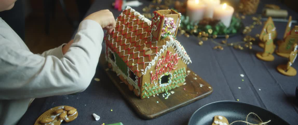 Boy decorating a gingerbread house with colorful cream icing at home