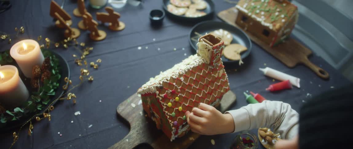 A person places candy on the roof of a gingerbread house