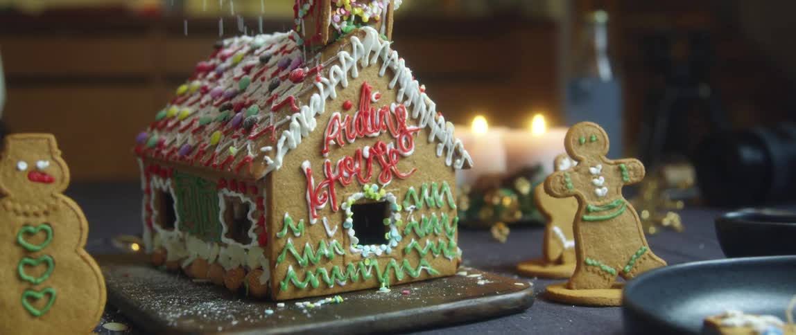 Powdered sugar is sprinkled over the top of a gingerbread house to mimic snow
