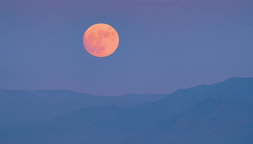 Full moon rising over mountains in a colorful sky