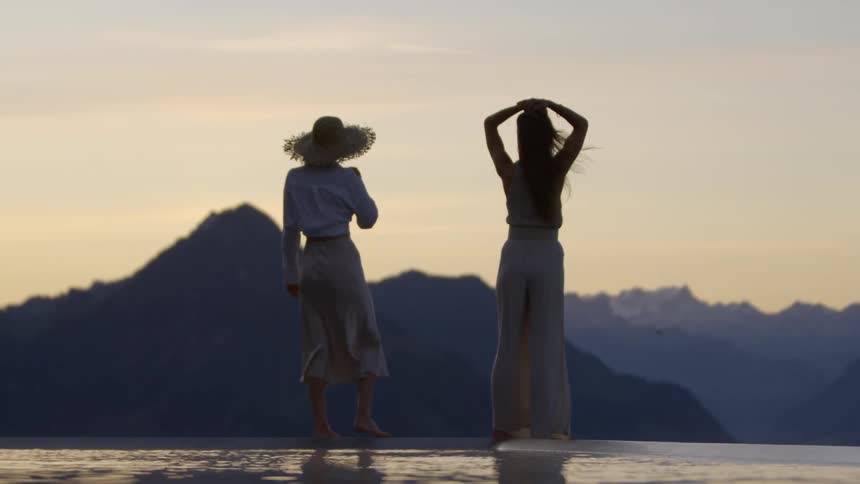 Two women stand in at the oceans edge to look out at the landscape at dusk