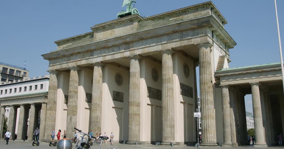 People on scooters and walking with a building with pillars in the background