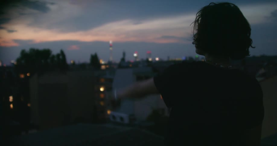 A woman stands outdoors looking at a city pointing with her fingers at nighttime