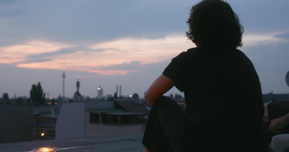 A woman sits outdoors on a rooftop while enjoying the early evening sky