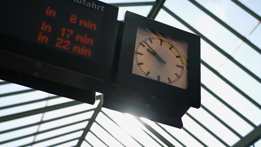 The sun shines on a clock attached to a sign