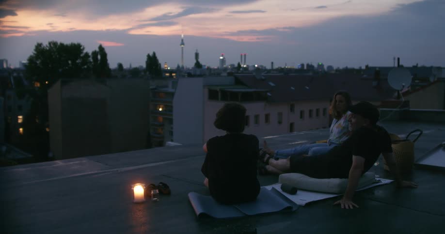 Three people are sitting on a roof at dusk