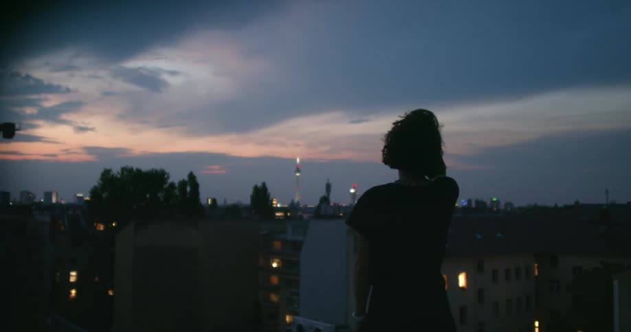 A man with a wristwatch standing on a rooftop with the city skyline the sky and clouds in the background