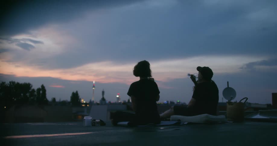 A group of people perform a toast and drink wine together on a rooftop in a city at sunset