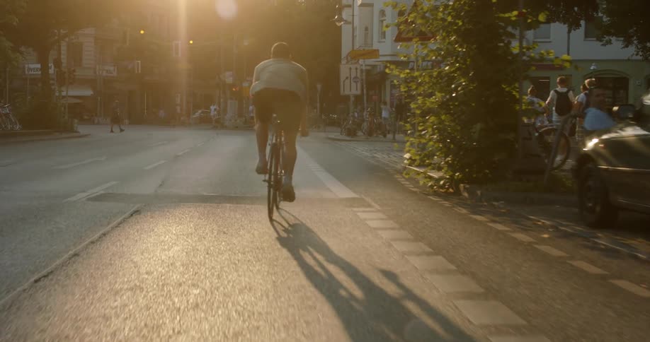 A man rides his bicycle down a city neighborhood street toward corner businesses