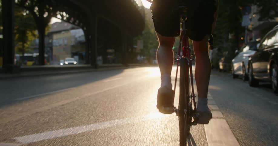 A person riding a bike on a city street with vehicles with buildings the sky and clouds in the background