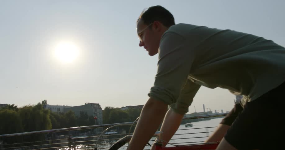 A man cycles across a bridge in a city