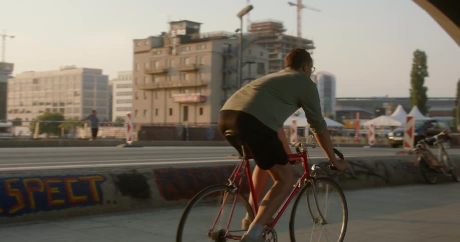 A man bikes on a sidewalk as cars and a bus drive alongside him