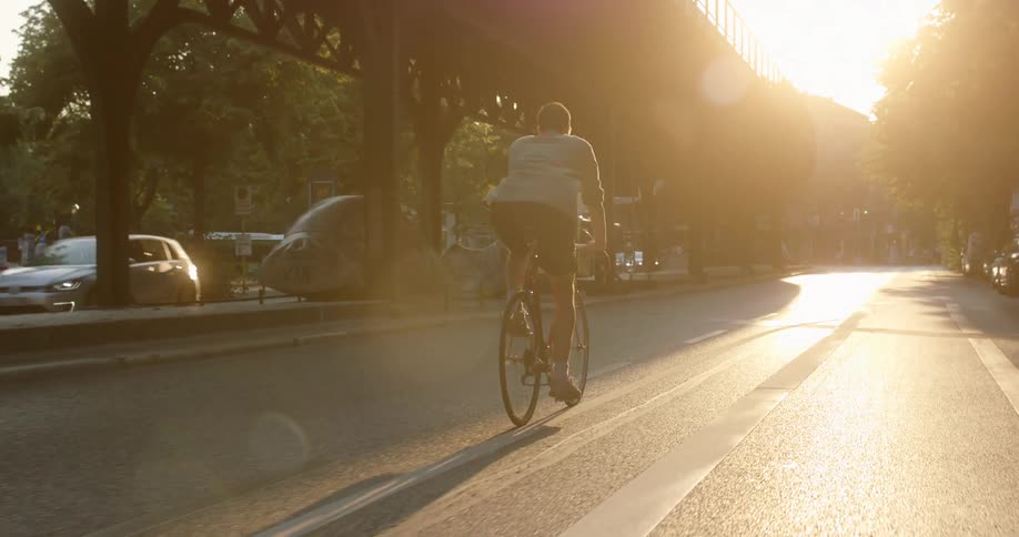 A man rides his bicycle down a neighborhood street that sits below a bridge and next to a park