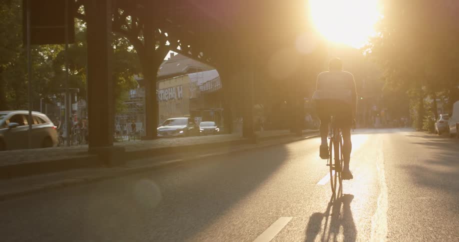 Person rides bike down road past cars at sunrise