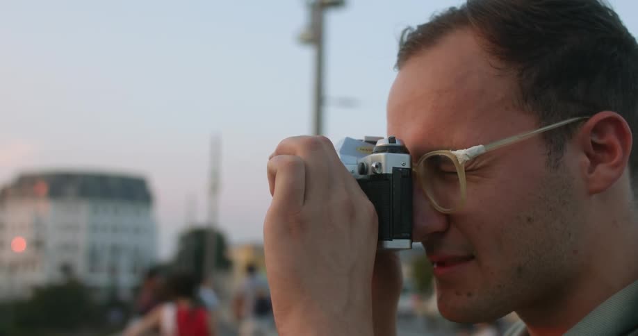 Man uses a vintage film roll camera to take pictures of the sunset in the city