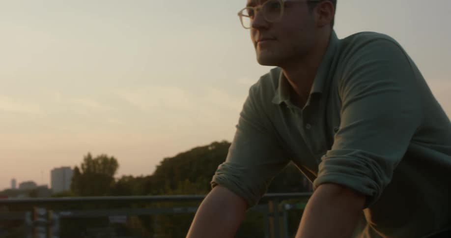 A man rides a bicycle across a bridge in a metropolis in the evening